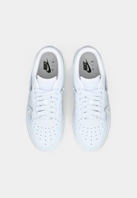 Et par hvite Nike Air-sneakers med snøring og perforert tåområde, vist fra oven på en lys bakgrunn.
