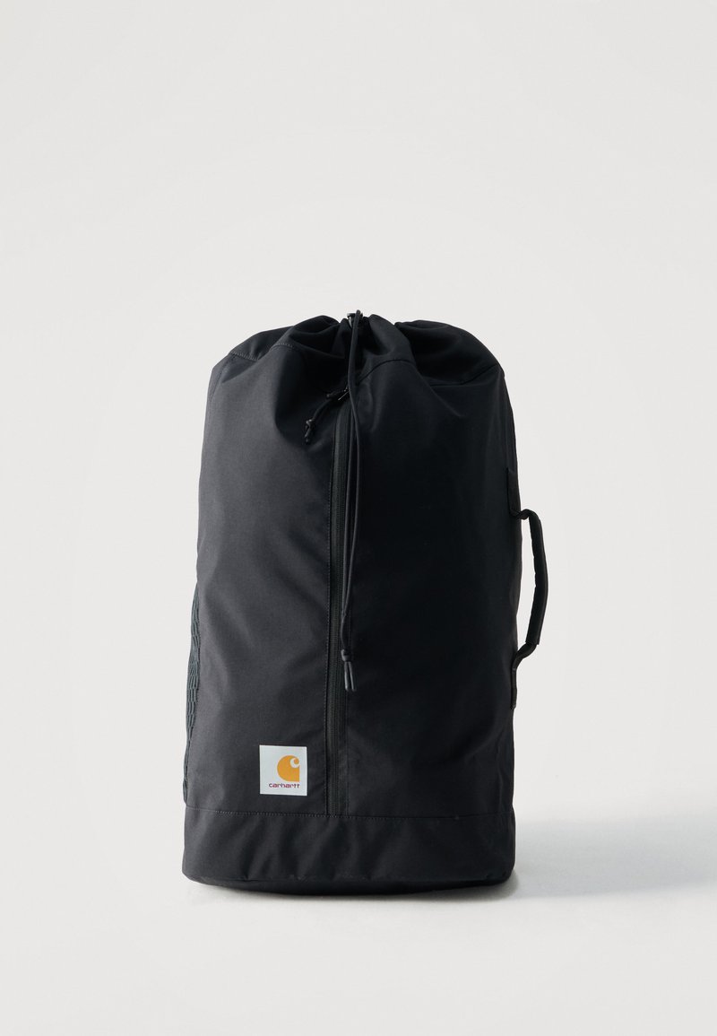 Μαύρη τσάντα ταξιδιού Carhartt με κλείσιμο με κορδόνι και πλευρική λαβή, όρθια σε απλό ανοιχτό φόντο.