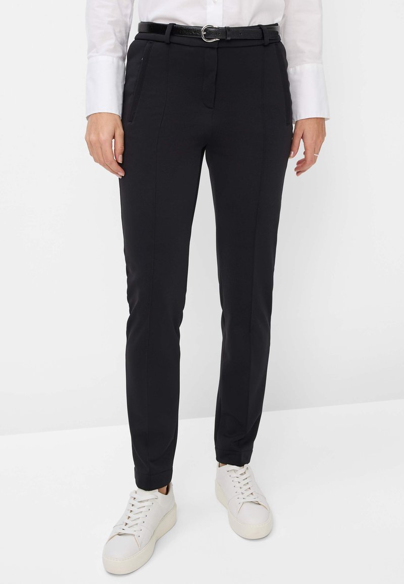 Schwarze maßgeschneiderte Hosen aus Stretchstoff, mit Seitentaschen, schmaler Passform und einem glänzenden schwarzen Gürtel mit einer runden Schnalle. Tragen Sie sie mit weißen Sneakers.