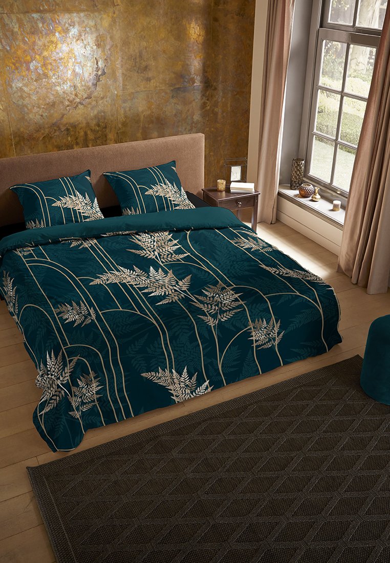 Ensemble de literie teal avec des motifs de fougères en crème, comprenant des taies d'oreiller assorties. Tapis à texture brune sur un sol en bois. Design doux et contemporain.
