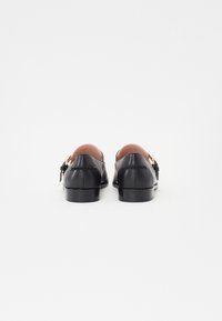 Black leather loafers with a rounded toe, low heel, and a brown leather lining. Features a gold buckle detail on the side.