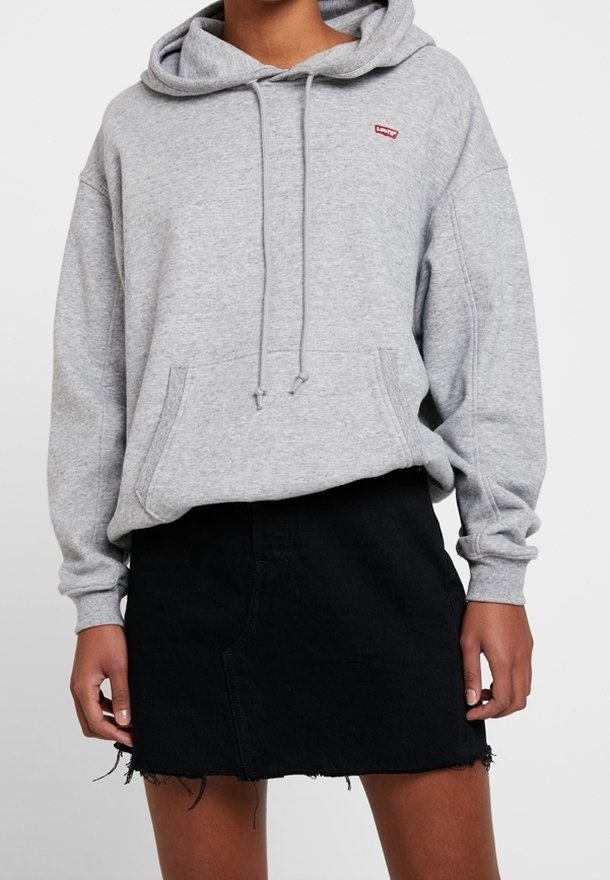 Hoodie gris avec un cordon de serrage, arborant un petit logo rouge, associé à une jupe en denim noir avec un ourlet effiloché. Texture douce, design décontracté.