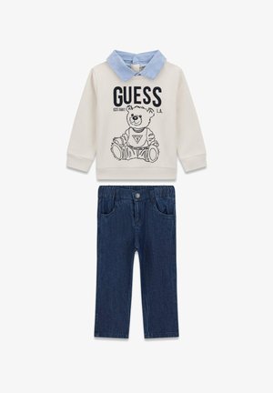 Hellbeiges Sweatshirt mit Jeanskragen und Bärengrafik; kombiniert mit dunkelblauen Jeanshosen mit Vordertaschen und elastischem Bund.