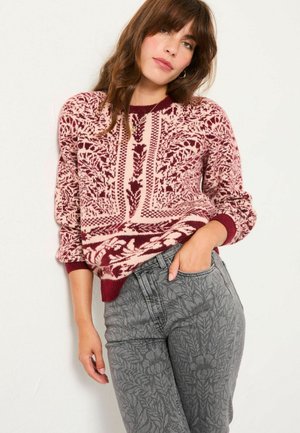 Strickpullover mit roten und rosa Blumenmustern, langen Ärmeln und rundem Halsausschnitt, kombiniert mit grauen Hosen mit blattähnlicher Textur.