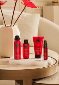 Cztery czerwone produkty kosmetyczne na marmurowej tacce: żel pod prysznic w pianie, nawilżający olejek do kąpieli, bitą śmietanę do ciała i mgiełkę do twarzy.