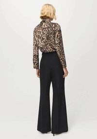 Blusa con stampa leopardata, maniche lunghe e colletto, abbinata a pantaloni neri a vita alta e gamba larga, che mostrano una texture liscia.
