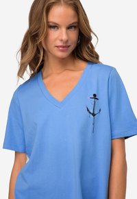 Blå bomulds V-hals T-shirt med et lille sort og lyserødt ankerdesign på venstre brystområde og korte ærmer. Blød tekstur.