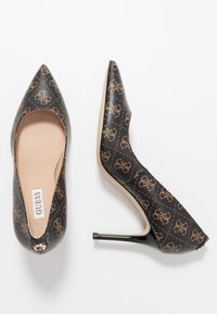 Escarpins à bout pointu en matière synthétique noire avec motif logo marron, intérieur beige lisse et talon brillant noir.