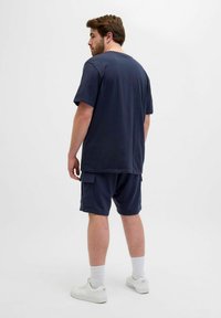 Navy Baumwoll-T-Shirt und passende Shorts mit Seitentaschen. Das Modell trägt weiße Sneakers und gerippte Socken. Schlichtes, lässiges Design.