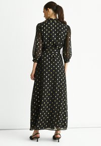 Black long dress with gold polka dots, sheer long sleeves, cinched waist, and a flowing silhouette. Smooth texture and ankle-length design.