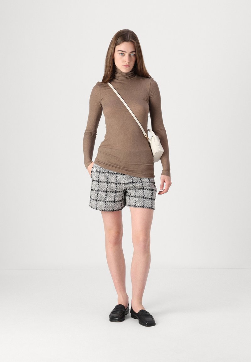 Braunes langärmliges Rollkragenoberteil kombiniert mit schwarz-weißen karierten Tweed-Shorts und schwarzen Slippern. Kleine Umhängetasche ruht auf der Schulter.