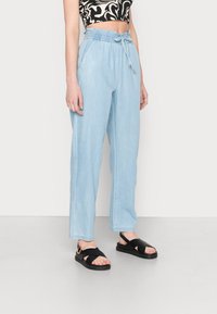 Light blue, loose-fitting pants with an elastic waistband and drawstring. Casual design features side pockets. Worn with black sandals.