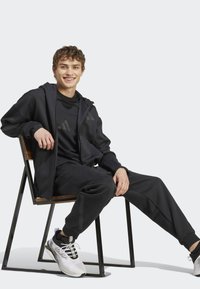 Fato de treino atlético preto feito de tecido suave, com um hoodie de fecho éclair, calças ajustadas e tênis leves com detalhes texturizados.
