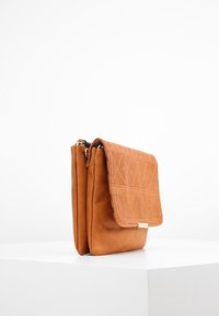 Tanfarvet læderhåndtaske med en tekstureret, mønstret klap. Rektangulær form med magnetlukning og et elegant design.