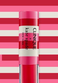 Clinique x Kate Spade lipproduct, cilindrisch, glanzend rode en roze gestreepte ontwerp, witte label met zwarte tekst, transparante basis.