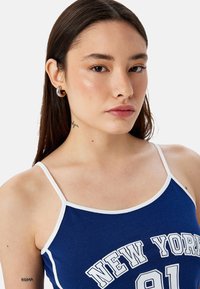 Blauwe tanktop met witte bies met de opdruk "NEW YORK 91". Gemaakt van zacht materiaal met een gladde textuur. Verstelbare spaghettibandjes.