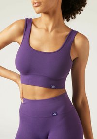 Lila ribbad crop top med en bred halsringning och tjocka axelremmar, i kombination med matchande högmidjade leggings. Diskret varumärkesetikett synlig.