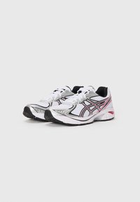 Scarpe sportive bianche con dettagli argentati, rifiniture nere, linee rosa e una parte superiore in mesh testurizzato. Presentano lacci bianchi piatti e una robusta suola nera.