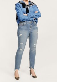 Lysblå denim skinny jeans med slidte detaljer, frynset kant, parret med en blå skjorte, sort-hvide stribede tørklæde og mønstrede hæle.