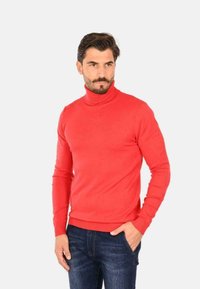 Maglione a collo alto rosso realizzato in tessuto liscio, dal design aderente, con maniche lunghe, polsini e orlo a coste, abbinato a jeans in denim blu.