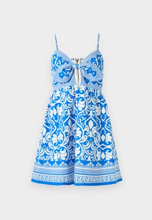 Robe bleue à motifs avec des designs floraux blancs, dotée de fines bretelles, d'un devant en forme de nœud et d'un corsage ajusté se terminant par une jupe évasée.