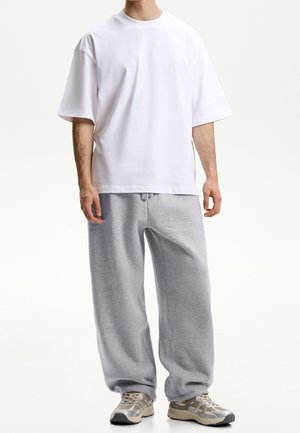 Weißes oversize Baumwoll-T-Shirt kombiniert mit hellgrauen Jogginghosen. Das Outfit zeichnet sich durch eine lockere Passform und einen Kordelzug an der Taille der Hose aus.