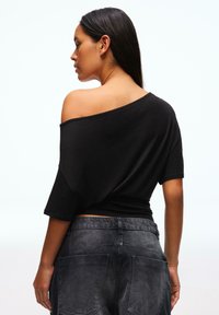 Fekete, vállakat szabadon hagyó, laza szabású felső rövid ujjakkal, magas derekú sötétszürke farmer rövidnadrággal, mely zsebekkel rendelkezik.