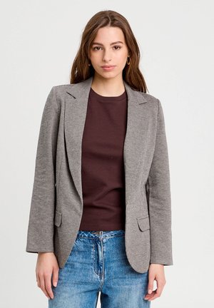 Gray checkered blazer with notched lapels, two front pockets, and a tailored fit, layered over a brown shirt and blue jeans.
