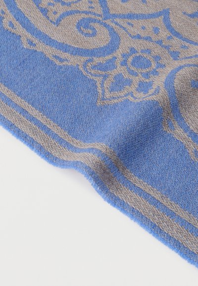 Coin de tissu tissé bleu et beige avec motif floral et tourbillons, bordure double rayée sur fond blanc.