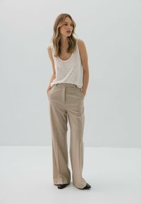 Biała bezrękawnikowa bluzka z okrągłym dekoltem, zestawiona z beżowymi, wysokim stanem spodniami o szerokich nogawkach, które mają delikatny wzór w kratkę. Czarne szpilki.