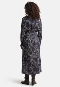 Μακρύ ναυτικό μπλε φόρεμα με λευκό ανθισμένο σχέδιο, με μακριά μανίκια, ζώνη στη μέση και αέρινη γραμμή. Φορεμένο με καφέ μπότες μέχρι το γόνατο.