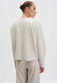 Beige, gestructureerde trui met een ontspannen pasvorm, voorzien van een ronde halslijn en lange mouwen, gedragen over lichte broek.