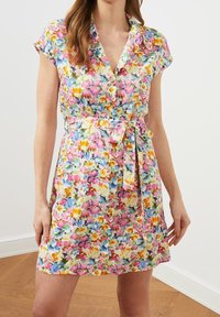 Sukienka w kwiaty z guzikiem, krótkimi rękawami, paskiem w talii oraz wielokolorowym wzorem na jasnym tle.