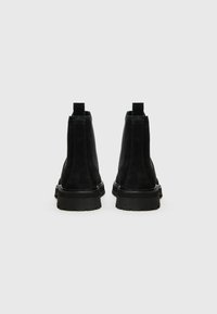 Botines Chelsea de ante negro con un acabado suave, punteras redondeadas y suelas de goma resistentes. Incluyen tiradores para facilitar su uso.