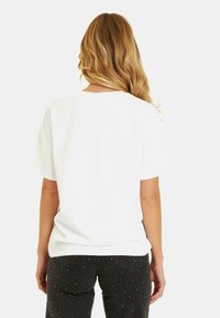 T-shirt en coton blanc avec des manches courtes, col rond, texture lisse. Associé à un jean noir avec des accents de brillance subtils.