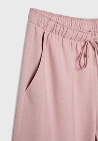 Pantalon rose clair avec une ceinture élastique et un cordon de serrage ajustable. Comprend des poches latérales et une texture lisse et douce.