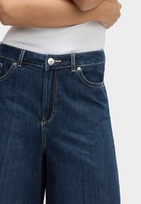 Dunkelblaue Denim-Jeans im geraden Schnitt, mit einem Knopf- und Reißverschluss, fünf Taschen und hellen Kontrastnähten.