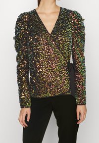 Top avvolgente nero con paillettes, scollo a V profondo, spalle texture e dettaglio in vita legato. Le paillettes hanno superfici riflettenti multicolori.