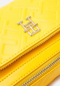 Borsa in pelle gialla trapuntata con un logo geometrico argentato. Presenta una chiusura con zip e una superficie liscia e testurizzata.