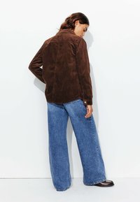 Veste en velours côtelé brun avec un tissu texturé, vue de dos. Associée à un jean large bleu clair, avec un léger délavage et une coupe décontractée.