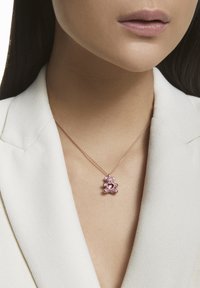 Rose gold necklace features a bear-shaped pendant with pink gemstones and a heart design, resting on a light-colored blazer.