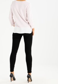 Světle růžový pruhovaný top s dlouhým rukávem, vrstvený přes bílé spodní oblečení, v kombinaci s černými skinny džíny a černými vysokými podpatky.