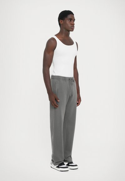 Gray sweatpants with drawstring waist, side pockets, and relaxed fit, paired with a fitted white tank top and black-and-white sneakers.