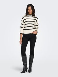 Randig polotröja i kräm och svart, kombinerad med tajta svarta jeans och eleganta svarta knähöga stövlar. Mjuk textur och modern passform.