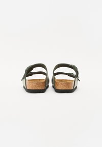Grønne sandaler med åben ryg, justerbare stropper, korkfodbed og tekstureret gummisål. Har en kvastdetalje nær stroppen.
