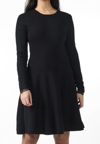 Robe noire à manches longues en matériau doux. Elle présente un corsage ajusté, une jupe évasée et des accents en dentelle sur les poignets.