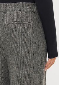 Pelēku dūmu raksta bikses ar plakanu jostu, sānu kabatām un aizmugures kabatu. Audumam ir teksturēta, austa izskata virsma.