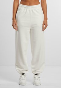Hvide bomulds-sweatpants med elastisk talje og manchetter, der har en afslappet pasform og sidelommer, matchet med hvide sneakers.