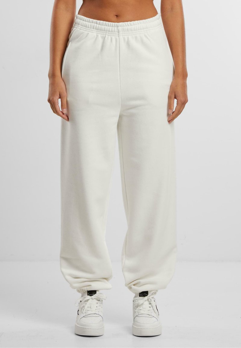 Hvide bomulds-sweatpants med elastisk talje og manchetter, der har en afslappet pasform og sidelommer, matchet med hvide sneakers.