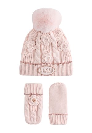 Un niño sonriente con un abrigo de invierno rosa, un gorro de punto con pompón y manoplas se lleva ambas manoplas a las mejillas.